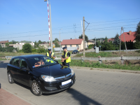 Policjantka Ruchu Drogowego kontroluje pojazd w rejonie przejazdu kolejowego. Obok stoi policjant asekurujący.