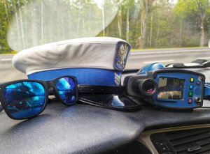 podszybie radiowozu, na nim okulary przeciwsłoneczne, policyjna czapka, oraz miernik prędkości